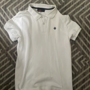 Vit pikétröja från Morris Stockholm - Klassisk vit pikétröja från Morris Stockholm i storlek S. Tröjan har korta ärmar, krage med knappar och en liten broderad logga på bröstet. Perfekt för en clean och stilren look. Tillverkad i mjuk bomull som känns skön mot huden,PRIS KAN DIKSUTERAS 