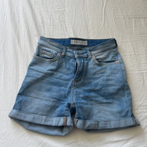 Blå jeansshorts från Newyorker, strl 36 - Snygga blå jeansshorts från Newyorker med klassisk femficksdesign och uppvikta benslut. Shortsen har normal passform och stängs med dragkedja och knapp. Perfekta för varma dagar och enkla att matcha med allt i garderoben.