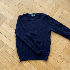 Mörkblå kashmirtröja Alan Paine - Mörkblå stickad tröja från Alan Paine i mjuk kashmir. Klassisk rund halsringning och ribbade muddar vid ärmslut och nederkant. Perfekt för lager-på-lager under höst och vinter. Enkel och stilren design som funkar till allt.