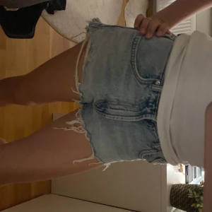 Ljusblå jeansshorts med fransar - Säljer ett par väldigt snygga ljusblå jeansshorts med råa, fransiga kanter och klassisk femficksdesign. Shortsen har en loose fit som ger en avslappnad vibe. Perfekta för sommardagar och festivaler. 