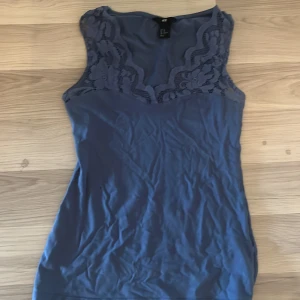 Blå linnetopp med spets från H&M - Supersöt blå linnetopp från H&M i storlek XS. Toppen har breda axelband och v-ringning med fina spetsdetaljer upptill som ger en romantisk vibe. Perfekt att styla med jeans eller kjol för en chill look.