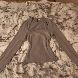 Grå långärmad topp från Divided - Säljer en stilren grå långärmad topp från Divided. Toppen har en snygg fyrkantig urringning och är figurnära i modellen. Perfekt att matcha med jeans eller kjol för en clean look.