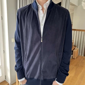 Mörkblå mocka bomberjacka Gran Sasso - Snygg mörkblå overshirt från Gran Sasso i mjuk mocka med ribbade muddar och krage. Jackan har dragkedja framtill och två fickor. Den är i bra skick och använd varsamt. Pris kan diskuteras.