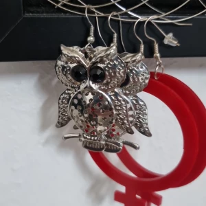 Silvriga uggleörhängen med svarta ögon - Coola stora örhängen i form av ugglor i silvrig metall med svarta ögon. Ugglorna har prickigt mönster på magen och är ca 5 cm långa. Sparsamt använda,  okänt material.