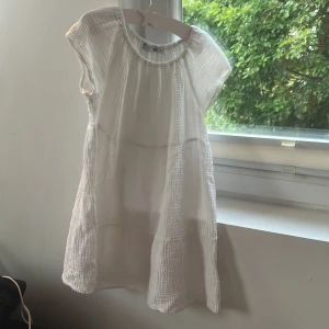 Vit kort sommarklänning från 157 - Luftig och söt vit kortklänning från lager  157 i storlek 130/140. Klänningen har korta ärmar, rund hals och är gjord i ett mjukt, strukturerat bomullstyg. Perfekt för varma dagar med sin enkla och avslappnade stil.