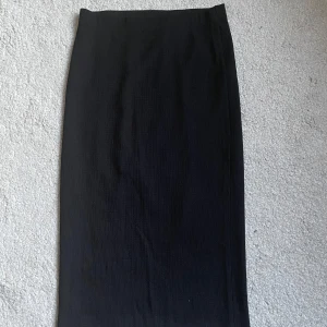 Svart långkjol från Vero Moda XS - Rak svart långkjol från Vero Moda i storlek XS. Kjolen har en enkel och stilren design med lätt ribbad struktur i tyget. Perfekt för dig som gillar minimalistisk och clean stil.