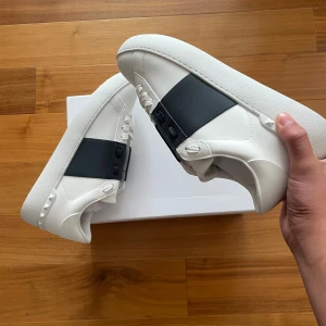 Valentino Garavani sneakers - Valentino Garavani Storlek 43  Vit med mörkblå detalj  Helt nya – aldrig använda  Helt nya sneakers från Valentino – aldrig använda  Stilrena, vita med mörkblå detalj, perfekt för sommaren  Kommer med allt: box, påse och dustbag  Exklusiva och svåra att få tag på 
