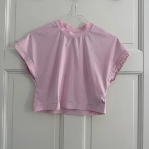 Ljusrosa croppad topp från SOC - Säljer en ljusrosa träningströja topp från SOC med ribbad rund halsringning. Toppen är ärmlös med breda axlar och har en enkel, stilren design. Perfekt för dig som gillar sportig och avslappnad stil.