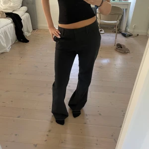 Mörkgråa kostymbyxor med bootcut - Jag är 170 bär vanligtvis S men dessa är 40. Sitter ändå bra. Snygga mörkgråa kostymbyxor med bootcut och normal passform. Byxorna har hällor för bälte och klassisk design med raka ben som får en lätt utsvängd siluett. Perfekta för en clean och stilren look.