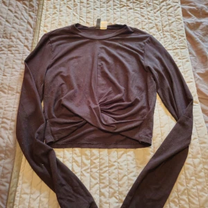 Svart croppad topp från H&M Divided - Säljer en svart långärmad croppad topp från H&M Divided. Toppen har en snygg twistad detalj framtill som ger en cool look. Mjuk och stretchig i materialet, perfekt att styla med höga jeans eller kjol.