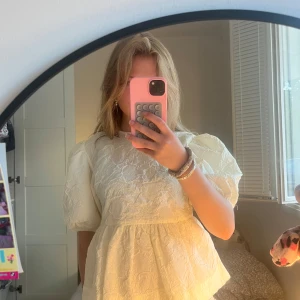 Vit blus med puffärmar och struktur - Supersöt vit blus med puffiga korta ärmar och strukturerat tyg med blommig känsla. Modellen är lite lös och har en lätt volang nedtill. Perfekt för dig som gillar romantiska och trendiga vibes.