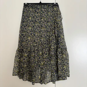 Blommig långkjol från Vero Moda XS - Supersöt långkjol från Vero Moda i svart med små gula och lila blommor. Kjolen har volangdetaljer och är gjord i ett lätt, flowy material som känns perfekt för vår och sommar. Resår i midjan för extra bekvämlighet. Använd en gång!