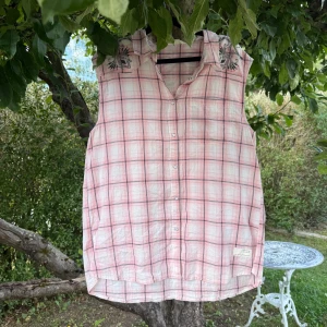 Rutig ärmlös skjorta i bomull - Säljer en luftig och ärmlös skjorta från Odd Molly med rosa och vita rutor, svarta linjer och broderade detaljer på kragen. Skjortan har knappar hela vägen och är gjord i tunn bomull, perfekt för varma dagar. Snygg och chill stil! Storlek 4 som enligt deras storleksguide motsvarar en storlek XL. Fint skick, men kan finnas någon liten anmärkning. 