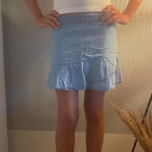 Ljusblå volangkjol med resårmidja - Supersöt ljusblå kortkjol med volangkant och bred resår i midjan. Kjolen har en enkel, flowy passform och är tillverkad i mjukt bomullstyg som känns skönt mot huden. Perfekt för dig som gillar en chill och feminin stil under varmare dagar.