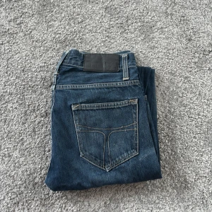 Blå jeans Tiger of Sweden 29/34 - Snygga blå jeans från Tiger of Sweden i klassisk straight fit. Jeansen har fem fickor, knappgylf och coola kontrastsömmar. Perfekt tvättad denim som ger en chill vibe och passar till allt. Materialet är slitstarkt jeans och färgen är mörkblå.
