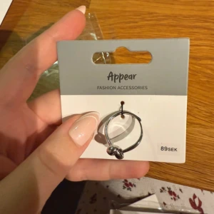 Silverfärgad ring med knut från Appear - Snygg och stilren ring i silverfärg från Appear, med en cool knutdetalj framtill. Ringen har en rund form och är perfekt för dig som gillar minimalistiska accessoarer med en twist. Passar till alla tillfällen och är lätt att matcha med andra smycken.