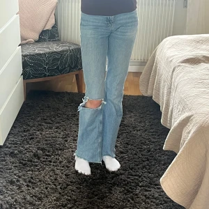 Blå jeans från g perfect jeans, storlek 32 - Säljer ett par ljusblå jeans från gina perfect jeans i storlek 32. Modellen har raka ben med råa, fransiga kanter och en sliten reva på ena knät för en cool, edgy vibe. Klassisk femficksdesign och midwaist passform. Perfekt för dig som gillar streetstyle.💗