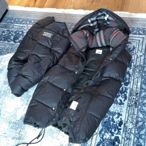 Svart Burberry pufferjacka med huva - Säljer en svart pufferjacka från Burberry med avtagbara ärmar och huva. Storlek M/S