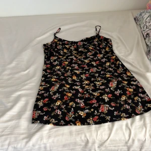 Blommig svart kortklänning MNG XS - Supersöt svart kortklänning från MNG Basics i storlek XS. Klänningen har tunna axelband och ett färgglatt blommigt mönster med inslag av rött, gult och vitt. Perfekt för dig som gillar en feminin och chill stil. Materialet känns lätt och skönt mot huden.