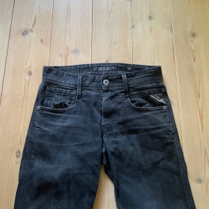 Svarta Replay jeans straight fit - Snygga svarta jeans från Replay med klassisk femficksdesign och raka ben. Jeansen har diskreta Replay-detaljer på fickorna och en patch bak i midjan. Materialet är slitstarkt denim i bomull och passformen är normal med midwaist. Perfekt för dig som gillar stilrena och tidlösa jeans.