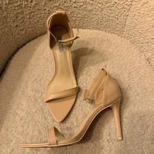 Beige klackskor med spetsig tå - Snygga beige pumps från NLY Shoes med CA 9 cm klack. Skorna har en tunn rem över tårna och en smal ankelrem med spänne. Glansig finish. Perfekta för dig som gillar stilrena och eleganta skor. Extra klacktoppar medföljer. Använda enstaka gång.