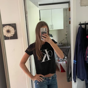 Svart croppad t-shirt från Calvin Klein - Storlek L men passar som xs/s Svart croppad t-shirt från Calvin Klein med stor vit CK-logga på bröstet. T-shirten har korta ärmar och rund hals. Materialet är mjuk bomull och passformen är loose, perfekt till jeans eller shorts.