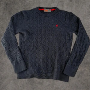 Mörkblå 100% Merinoull kabelstickad tröja Morris M - Mörkblå kabelstickad tröja från Morris i 100% merinoull. Klassisk rund hals och långärmad modell med röd broderad logga på bröstet. Snygg ribbad kant vid ärmslut och nederkant. Perfekt för dig som gillar stilrena och tidlösa plagg. Den passar mer som Xs Den har ett litet täcken på användning som man ser på bilden men det är ej något som syns eller märks, Dm vid frågor🙌