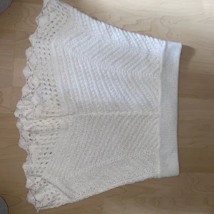 Vit stickad kjol från River Island - Supersöt vit stickad kjol från River Island med volangkant och snyggt mönstrad struktur. Kjolen är kort och har en bred, bekväm midjeresår. Perfekt för dig som gillar romantiska detaljer och vill ha en unik look.