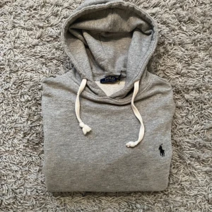  Polo Ralph Lauren hoodie - Snygg grå hoodie från Polo Ralph Lauren med klassisk svart broderad logga på bröstet. Inget smuts eller defekter. Pris kan diskuteras vid snabb affär.