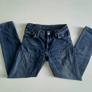 Mörkblå jeans från Nudie Jeans Co - Säljer ett par mörkblå jeans från Nudie Jeans Co i klassisk femficksmodell. Jeansen är lite små i storlek. Jeansen har raka ben, slim passform och snygga detaljer med kontrastsömmar på bakfickorna. Perfekt för dig som gillar stilrena och tidlösa jeans.