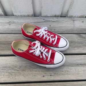 Röda Converse All Star sneakers - Säljer ett par klassiska Converse All Star sneakers i rött med vit tå och vita snören. Lågt skaft, rund tå och platt sula. Skorna är i canvas med gummisula och har snygga kontrastsömmar. Perfekt för dig som gillar retrostil och vill sticka ut med färg. Nästan aldrig använda därför som nya! 