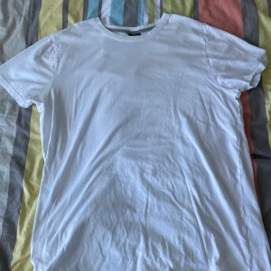 Vit t-shirt från Alphar One XXL - En klassisk vit t-shirt från Alphar One i storlek XXL. Modellen har rund hals och korta ärmar, perfekt för en clean och enkel stil. Tillverkad i mjuk bomull som känns skön mot huden. Passar dig som gillar basic och oversized vibe.
