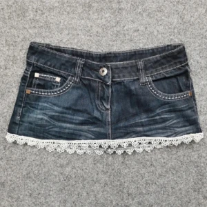 Jeanskjol med spetskant - Mörkblå jeanskjol i kort modell med snygga slitningar och vit spetskant längst ner. Klassiska fickor fram och bak, en bakficka med dragkedja. Perfekt för dig som gillar denim med en söt twist.