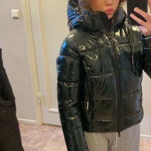 Grön glansig pufferjacka från Khujo - Säljer en glansig grön pufferjacka från Khujo med huva och snygga snören. Jackan har quiltad design, dragkedja framtill och logotyp på ärmen. Endast använd tre gånger så i princip nu, nypris ca. 2000kr