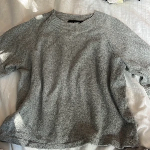 Grå stickad tröja från Vero Moda - Mysig grå stickad tröja från Vero Moda i storlek XS. Tröjan har en rund halsringning och långa ärmar med ribbade muddar.