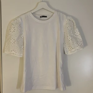 Vit blus med broderade puffärmar Zara - Superfin vit blus från Zara med puffiga kortärmar i broderad bomull och blommönster. Rund halsringning och rak passform. Perfekt för dig som gillar romantiska detaljer och vill ha en söt topp till jeans eller kjol.