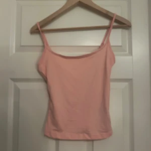 Ljusrosa linnetopp med smala axelband - Säljer en ljusrosa linnetopp med smala axelband och enkel design. Toppen är ärmlös och har en mjuk, lätt form som passar perfekt till varma dagar. Materialet känns som bomull och färgen är söt och fräsch. Perfekt att styla med jeans eller shorts.