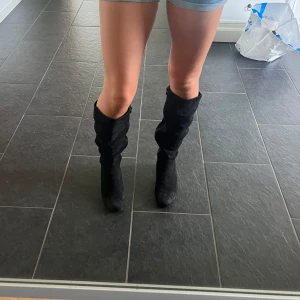 Svarta mockastövlar med klack - Säljer ett par svarta stövlar i mjuk mocka med rund tå och stabil klack. Stövlarna har dragkedja på insidan och en slouchy passform. Lite smutsiga på bilderna men går bort i tvätten.