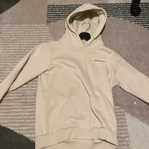 Beige hoodie från Peak Performance - Säljer en stilren beige hoodie från Peak Performance med broderad logga på bröstet. Tröjan har huva, ribbade muddar och en mjuk insida i fleece. Perfekt för chill dagar och har en klassisk passform med långa ärmar.