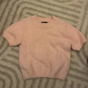 Ljusrosa stickad tröja Gina Tricot - Superfin ljusrosa stickad tröja från Gina Tricot i storlek S. Tröjan har korta ärmar, rund hals och breda ribbade muddar vid ärmslut och nederkant. Perfekt att styla med jeans eller kjol för en chill look.