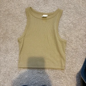 Glittrig guldig croppad linnetopp - Snygg croppad linnetopp i guld med glittriga detaljer och ribbad struktur. Toppen är ärmlös och har en stilren, rak form som passar perfekt till jeans eller kjol. Materialet är mjukt och stretchigt, vilket gör den superbekväm att bära. Storlek xs💓