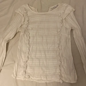 Vit blus med volang från KappAhl - Säljer en vit blus från KappAhl i storlek 38. Blusen har långärmade ärmar, tunna ränder och dekorativa volanger längs axlar och framstycke. Materialet känns lätt och luftigt, perfekt för vår och sommar. Snygg att matcha med jeans eller kjol!nöstan aldrig använt