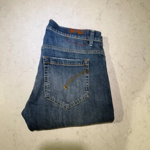 Dondup - Säljer ett par klassiska blå Dondup George med snygga slitningar och lätt tvättad look. Jeansen har fem fickor, orangea sömmar och en slim passform som sitter schysst på benen. Perfekt för dig som gillar en avslappnad men stilren vibe.- OBS! slitningarna är från köp- Nypris:2 999-Använts fåtal gånger!