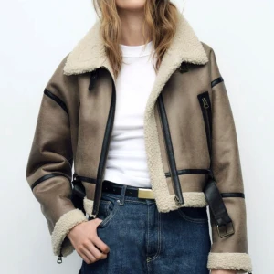 Beige teddyjacka med detaljer -  Jackan har svarta detaljer och spännen, samt dragkedja framtill. Croppad passform som ger en cool och trendig look.  Köpte den för 879kr Som en ny aldrig använt