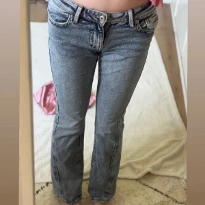 Low waist jeans från Gina Tricot - Snygga blå bootcut jeans med klassisk femficksdesign och broderade detaljer på bakfickorna. Jeansen har låg midja och är tillverkade i ett slitstarkt denimtyg som ger en cool vintagekänsla. Perfekta för dig som gillar en avslappnad men trendig stil. Modellen är Twisted jeans!