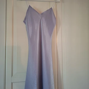 Vintage Ljuslila långklänning från Lulu H Paris - Säljer en elegant ljuslila långklänning från Lulu H Paris. Klänningen har smala axelband, v-ringad hals och ärmlös design. Materialet är glansigt och har ett mjukt fall som ger en lyxig känsla. Fin som balklänning eller bröloppsgäst möjligen