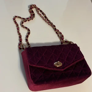 Vinröd axelväska med gulddetaljer – trendig & stilren - Elegant vinröd axelväska med kedja och guldfärgade detalje. Perfekt för dig som gillar att sticka ut med accessoarer❣️
