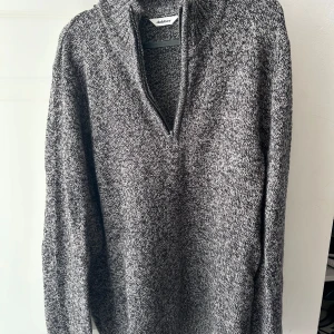 Gråmelerad stickad tröja Dobber - Säljer en gråmelerad stickad tröja från Dobber med halv dragkedja och v-ringad krage. Tröjan har lång ärm och är tillverkad av bomull, polyamid och ull. Perfekt för dig som gillar chill och enkel stil med lite edge.