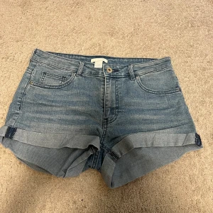 Blå jeansshorts från H&M, strl 36 - Snygga blå jeansshorts från H&M i storlek 36. Klassisk femficksmodell med uppvikta ben och knappstängning fram. Shortsen har normal passform och är gjorda i mjukt denimtyg som är perfekt för varma dagar.