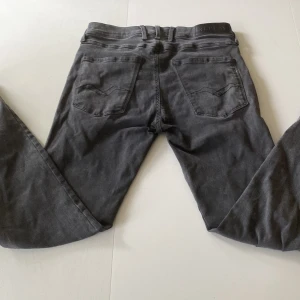 Mörkgråa replay jeans slim-fit  - Säljer ett par svarta jeans från Replay med klassisk femficksdesign och snygga detaljer på bakfickorna. Jeansen har en tapered passform som sitter smalt över låren och blir smalare nedtill. Materialet är mjukt jeans och färgen är mörk svart.